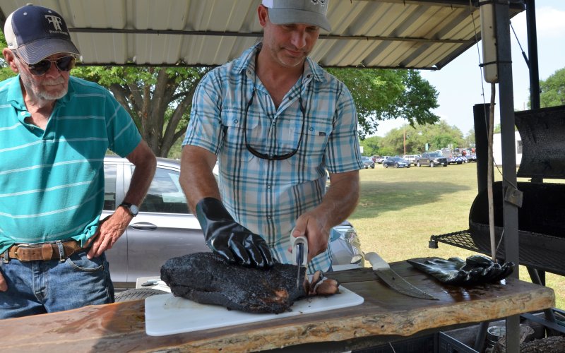 Kenneth Miller (left) watches as Jamey McCurry slices into brisket prepared by the Old School Cookers on Saturday, May 21.