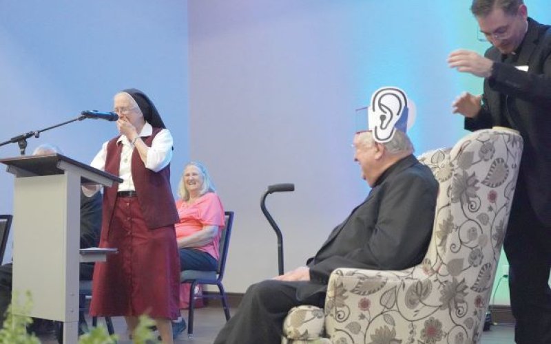 Sister Colette Kouba giggles at the mic after placing a pair of big paper ears on Monsignor John as part of the Roast and Toast event in Victoria earlier this month. Photo by Janet Jones/The Catholic Lighthouse