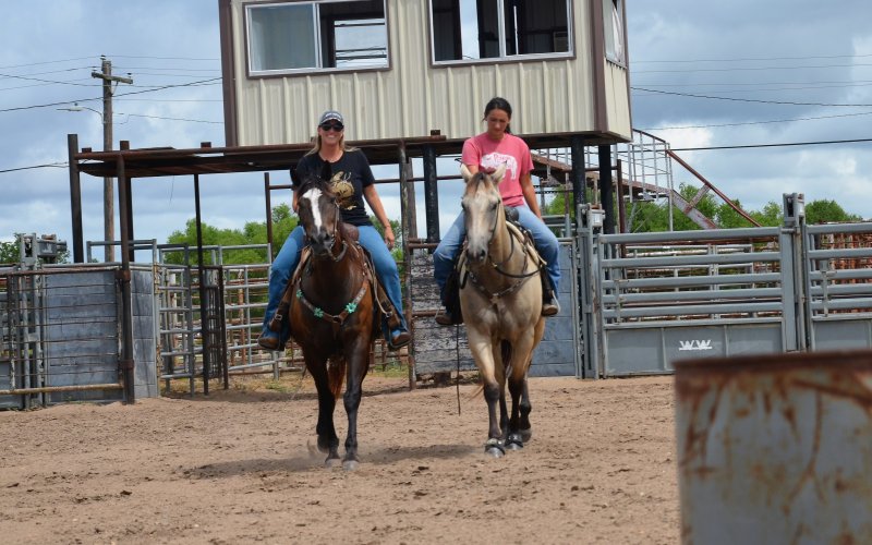 Kim Chandler (left) and Brittani Richter ride through the Yoakum Rodeo Arena on horseback Friday, July 12.