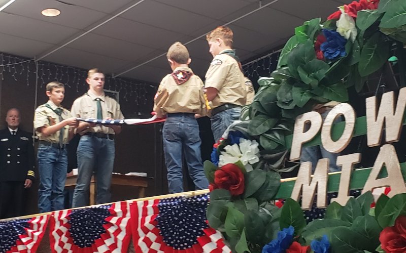 The POW/MIA wreath, of which Vietnam had more than its fair share for American troops, stands in silkent reminder while a Boy Scout troop performs a flag folding ceremony in the background during a recent Hallettsville veteran's appreciation event.