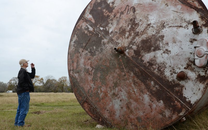 An unclaimed tank towers over DeWitt County Commissioner Precinct 1 Curtis Afflerbach on private property north of State Highway 72 on Thursday, Dec. 1.
