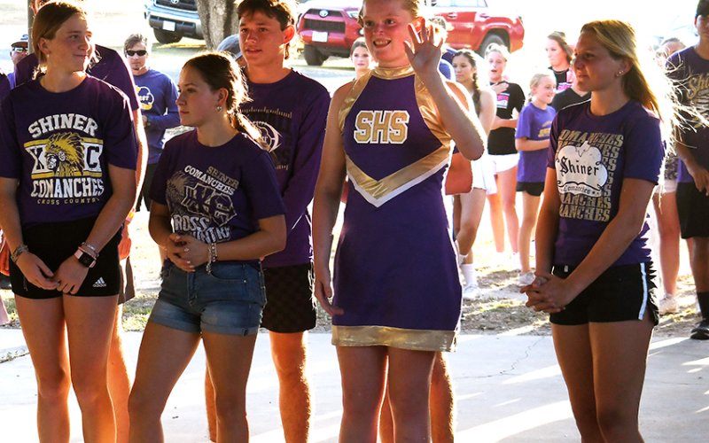 Lady Comanche cross-country runner Eve Roberts (second from right) waves to the crowd during the team’s introduction by head coach Michelle Winkenwerder at Meet the Comanches on Aug. 7. Photo by Mark Lube.