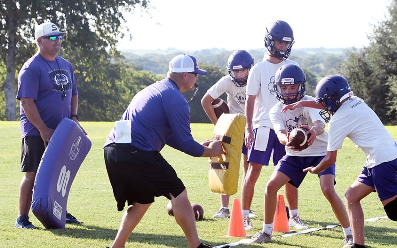 Shiner football coaches Jason Keller (far left) and Daniel Boedeker (second from left) put the Comanche offense through some triple option drills Monday evening. Photo by Mark Lube.