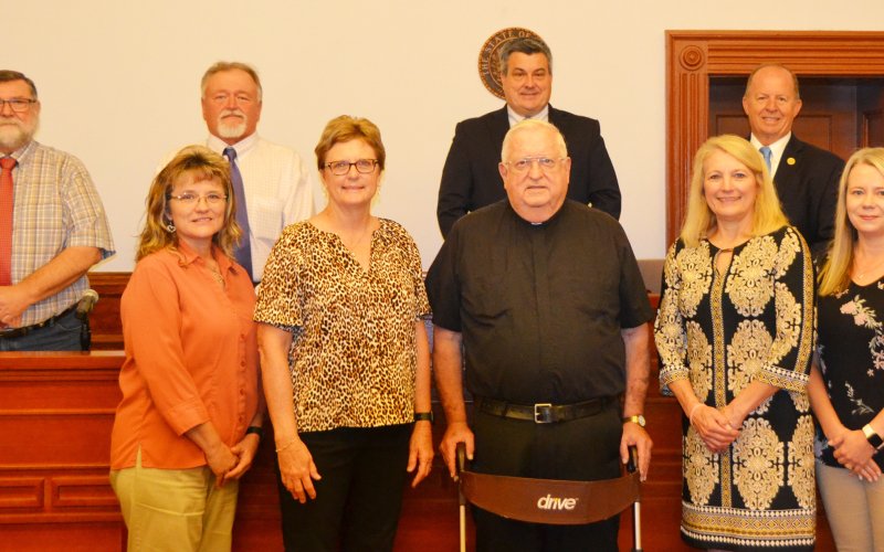 Sacred Heart Catholic Church pastor Msgr. John Peters was recognized with a proclamation reading at Monday’s Commissioner’s Court meeting. Msgr. John, who is retiring at the end of the month, served as a priest for 50 years and was the Sacred Heart pastor for the past 30 years. Front row, left to right, are Tammy Koerth (county treasurer), Barbara Steffek (county clerk), Msgr. John Peters, Deborah Sevcik (county tax assessor/collector, and  Lori Wenske (district clerk); back row, left to right, are commissi