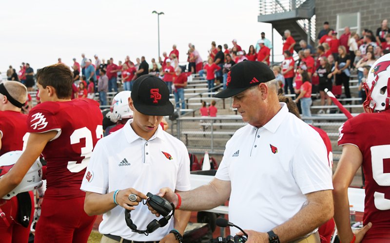 St. Paul assistant football coach Gerard Nunez (middle) and head coach Barry Wolf (right) double check their headsets before the game against CC John Paul II on Sept. 13.   Photo by Mark Lube.