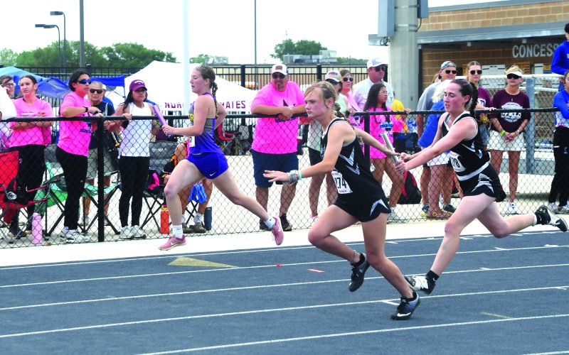 Karsyn Blahuta (left) accepts the handoff from Addison Simper during the 400-meter relay.  The Kittens advanced to state with second place in a time of 52.88 seconds.  Photo by Mark Lube.