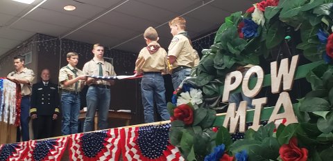 The POW/MIA wreath, of which Vietnam had more than its fair share for American troops, stands in silkent reminder while a Boy Scout troop performs a flag folding ceremony in the background during a recent Hallettsville veteran's appreciation event.