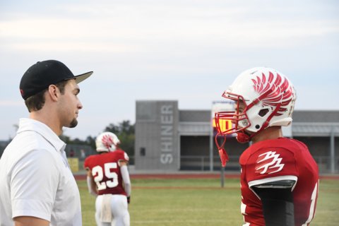 Defensive coordinator Ryan Geiger confers with a player before the game. Photo by Mark Lube.