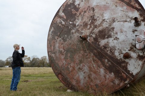 An unclaimed tank towers over DeWitt County Commissioner Precinct 1 Curtis Afflerbach on private property north of State Highway 72 on Thursday, Dec. 1. 