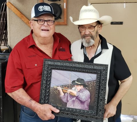 Kenneth Henneke, one of the founders of the annual Fiddlers Frolics in Hallettsville, poses with Keith Junot shortly after his Hall of Fame induction at the 50th annual Frolics held in 2021. Junot played what becanme the very first Frolics held at Wied Hall when he was just 12, already impressing those gathered with his talents. He clutches a potrait of him as a younger man that Sheridan artist Dennis Pesek painted presented to him at his induction ceremony.