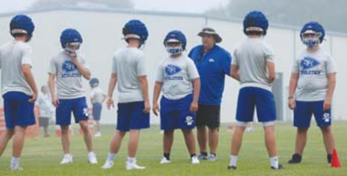 Photo by Chuck Grafe Head coach Rodney works with linemen during the first workout Monday morning.