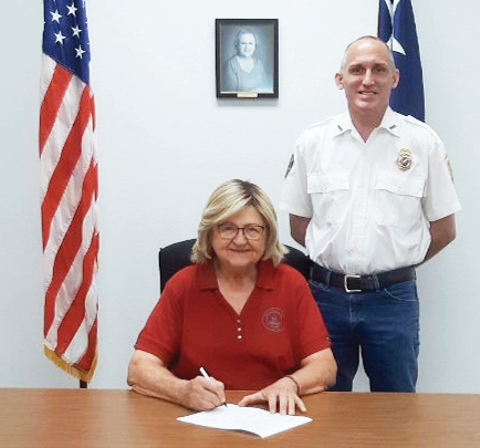 Fire Prevention Week is Oct. 4 through 10 and this year’s theme is “Charge into Fire Safety: Safe Charging  is a Superpower.” The week focuses on the proper ways to stay safe whencharging electronic devices that  contain a lithium-ion battery. Seated is Hallettsville mayor Alice Jo Summers, who signs a proclamation  naming the week, Fire Prevention Week. Witnessing the signing is Hallettsville VFD fire chief Stephen  Grahmann. Contributed photo