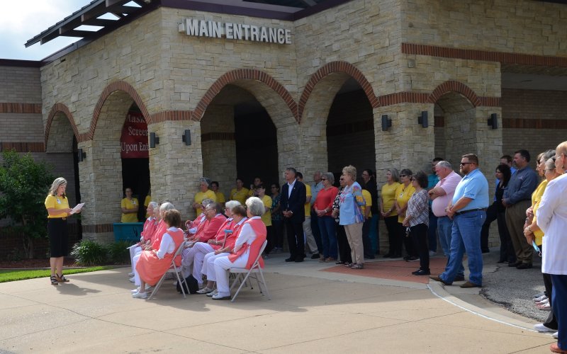 Attendees stand outside the Yoakum Community Hospital while Stephanie Lerch explains the hospital’s history.