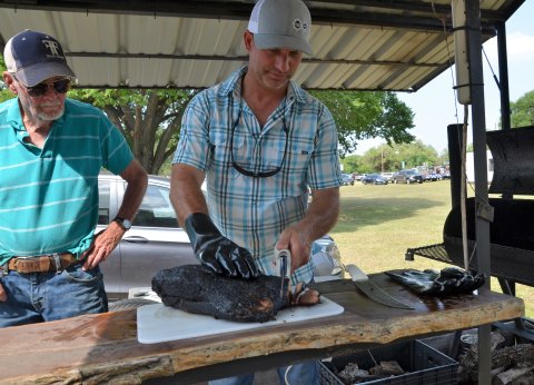 Kenneth Miller (left) watches as Jamey McCurry slices into brisket prepared by the Old School Cookers on Saturday, May 21.