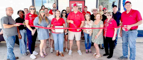 Jon and Renee Lamson, center of photo, prepare to cut a ribbon declaring their office location for American Shield Roofing and Construction, LLC. The ribbon cutting ceremony was held Friday afternoon with a number of friends and supporters attending the event. The office is located at 100 N. Texana St. in Hallettsville. Contributed photo